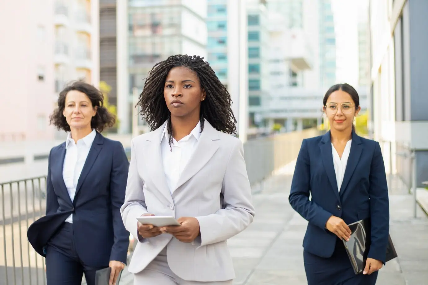 Selbstbewusste Teamleiterin hält beim Spaziergang ein Tablet. Selbstbewusste Geschäftsfrauen in Anzügen gehen die Straße entlang. Konzept der Teamarbeit.
